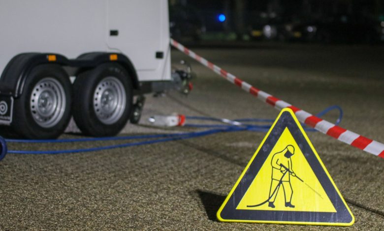 A construction warning sign and caution tape at night near a trailer, indicating ongoing work.
