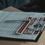 A clipboard with delivery papers and a 'Handle with Care' sticker on a cardboard box.