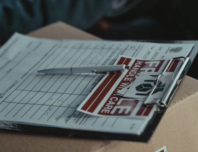 A clipboard with delivery papers and a 'Handle with Care' sticker on a cardboard box.