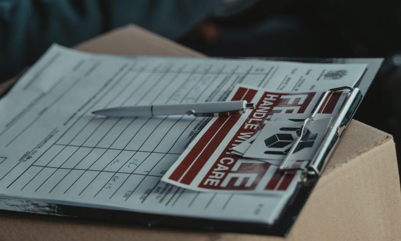 A clipboard with delivery papers and a 'Handle with Care' sticker on a cardboard box.