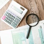 Tax forms laid out with a calculator and magnifying glass on a wooden surface, perfect for finance themes.