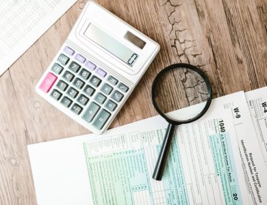 Tax forms laid out with a calculator and magnifying glass on a wooden surface, perfect for finance themes.