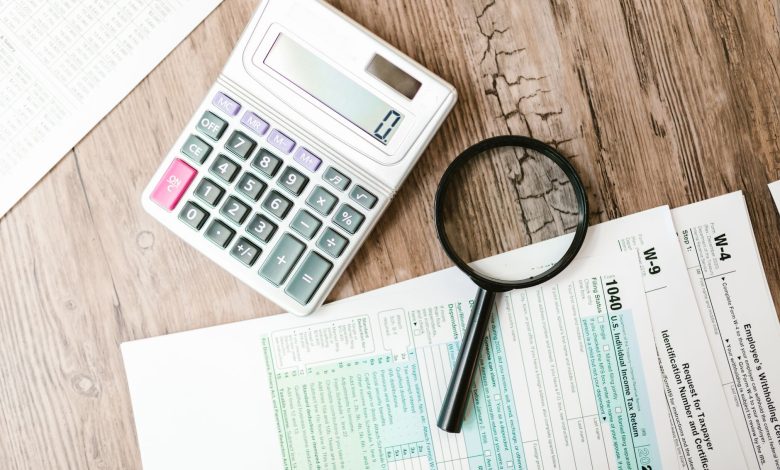 Tax forms laid out with a calculator and magnifying glass on a wooden surface, perfect for finance themes.