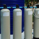Four beige tanks in an outdoor water treatment setup with blue piping.