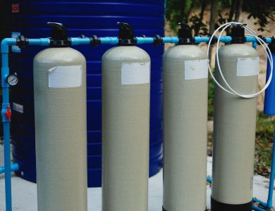 Four beige tanks in an outdoor water treatment setup with blue piping.