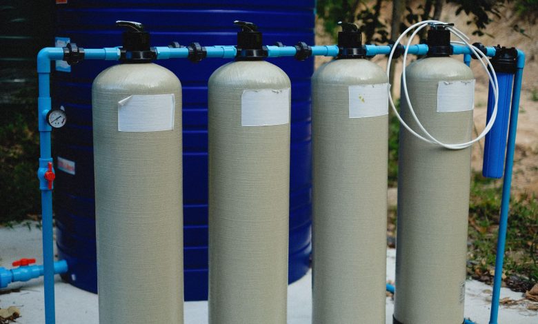 Four beige tanks in an outdoor water treatment setup with blue piping.