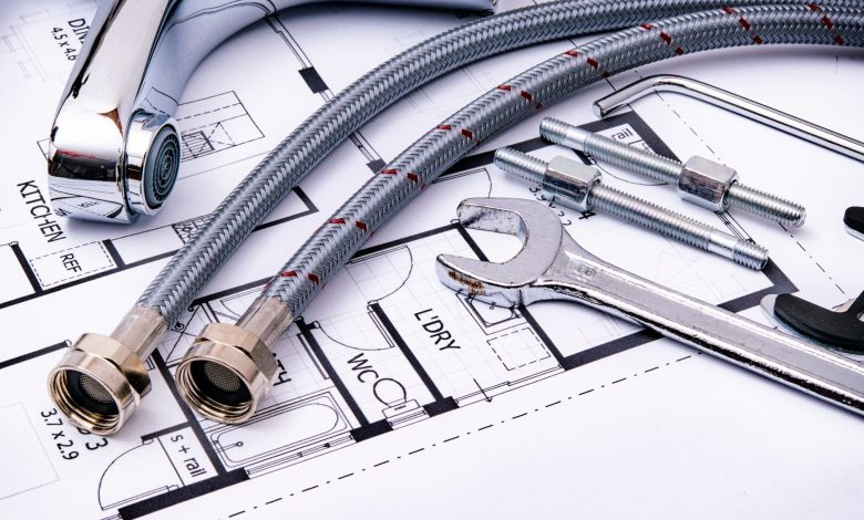 Close-up of plumbing tools and faucet on top of an architectural blueprint, perfect for hardware and construction themes.