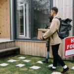 Young couple moving into a new rental home with boxes. Outdoor scene with a rental sign.