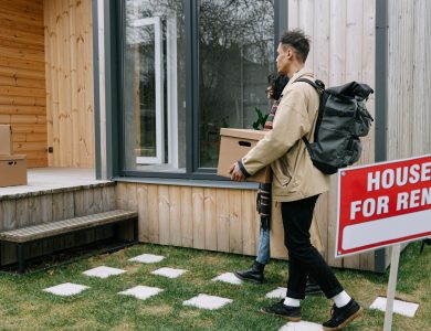 Young couple moving into a new rental home with boxes. Outdoor scene with a rental sign.