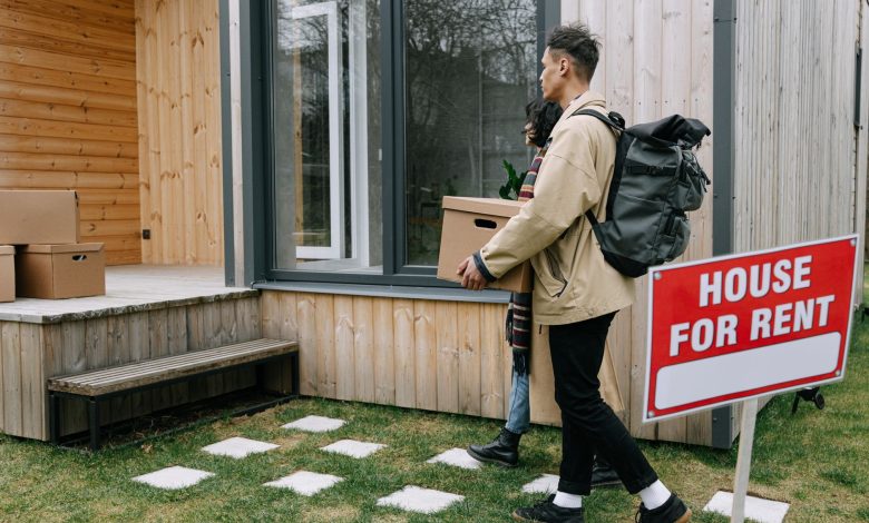 Young couple moving into a new rental home with boxes. Outdoor scene with a rental sign.