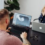 Two professionals working on laptops, engaging in a collaborative office environment.
