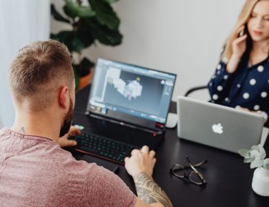 Two professionals working on laptops, engaging in a collaborative office environment.