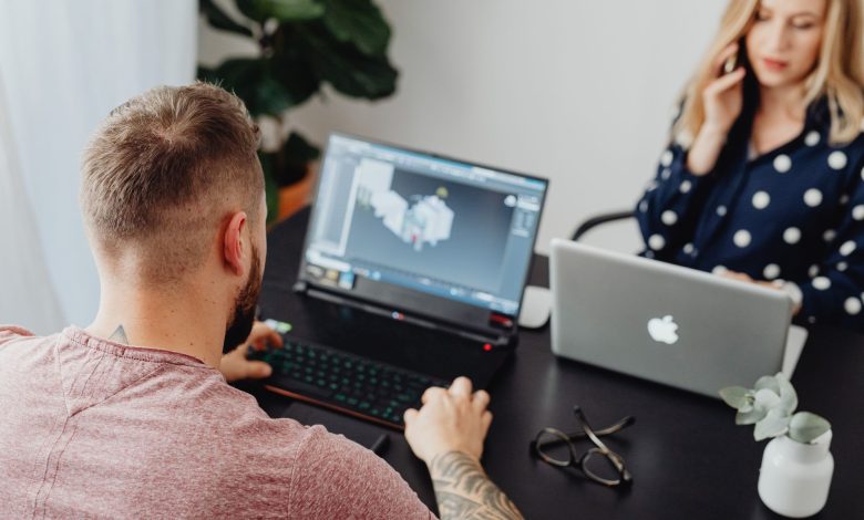 Two professionals working on laptops, engaging in a collaborative office environment.