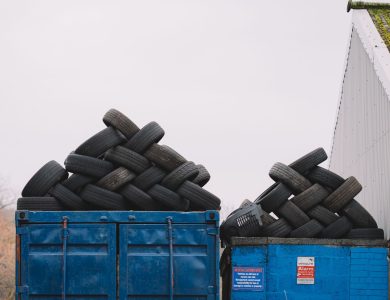 Piles of used tires on blue containers in an industrial recycling yard.
