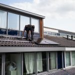 Technician working on installing solar panels on a residential rooftop during the day.