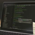 A close-up of a laptop displaying code in a dimly lit room with a coffee mug nearby.