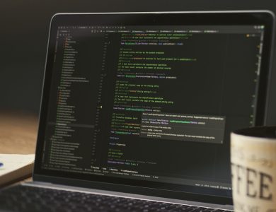 A close-up of a laptop displaying code in a dimly lit room with a coffee mug nearby.