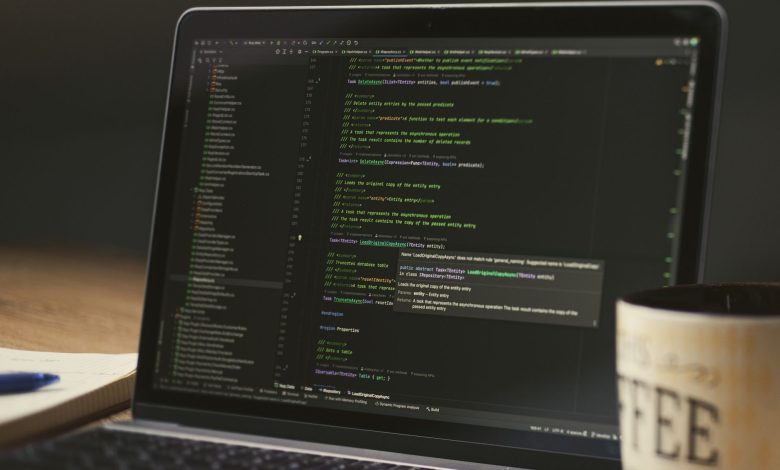 A close-up of a laptop displaying code in a dimly lit room with a coffee mug nearby.
