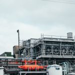 Industrial factory with metal pipes and special equipment surrounded with fences located against cloudy sky on street with power lines in town