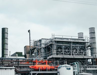 Industrial factory with metal pipes and special equipment surrounded with fences located against cloudy sky on street with power lines in town