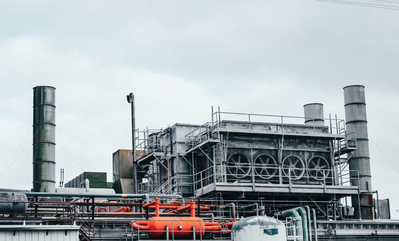 Industrial factory with metal pipes and special equipment surrounded with fences located against cloudy sky on street with power lines in town