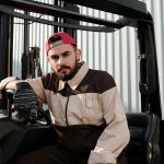 Focused forklift operator in uniform seated in industrial setting, showcasing work environment.