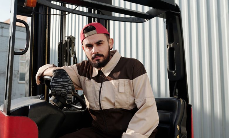 Focused forklift operator in uniform seated in industrial setting, showcasing work environment.
