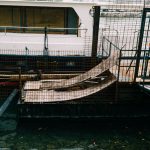 A boat moored at a dockside in an industrial setting, featuring metal railings and ramps.