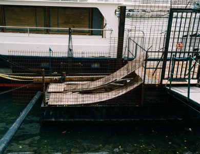 A boat moored at a dockside in an industrial setting, featuring metal railings and ramps.