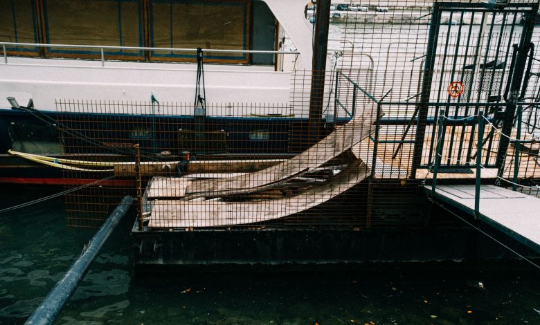 A boat moored at a dockside in an industrial setting, featuring metal railings and ramps.