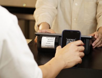 Two individuals engaged in a contactless payment using a QR code scanner at a retail counter.