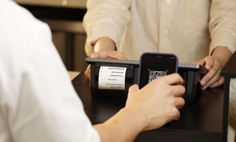 Two individuals engaged in a contactless payment using a QR code scanner at a retail counter.