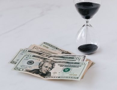 From above of transparent glass with black sand on white table and pile of paper money with image of president