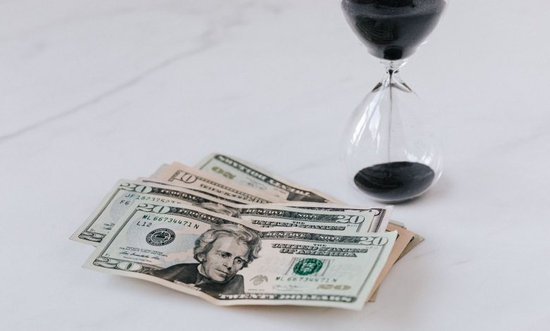 From above of transparent glass with black sand on white table and pile of paper money with image of president