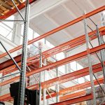 Bright warehouse interior with orange metal shelving units and stored goods.