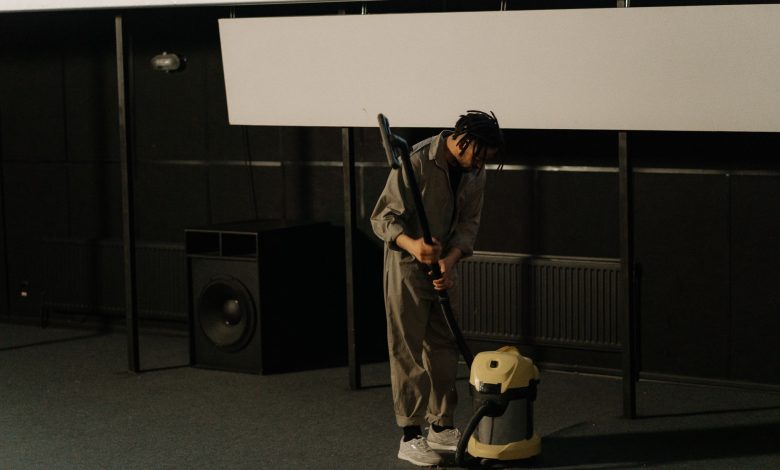 A person in uniform using a vacuum cleaner inside an auditorium with a visible speaker.