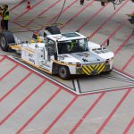 Aircraft tug maneuvering on a runway, preparing for plane departure at a busy airport.