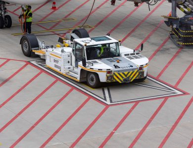 Aircraft tug maneuvering on a runway, preparing for plane departure at a busy airport.