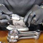 Close-up of a technician's hands assembling a metal connecting rod with precision and care.