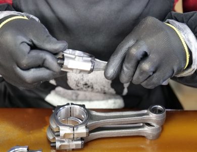 Close-up of a technician's hands assembling a metal connecting rod with precision and care.