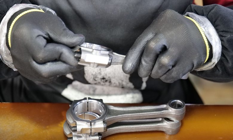 Close-up of a technician's hands assembling a metal connecting rod with precision and care.
