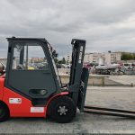 Red industrial forklift parked in a dockyard with urban background.