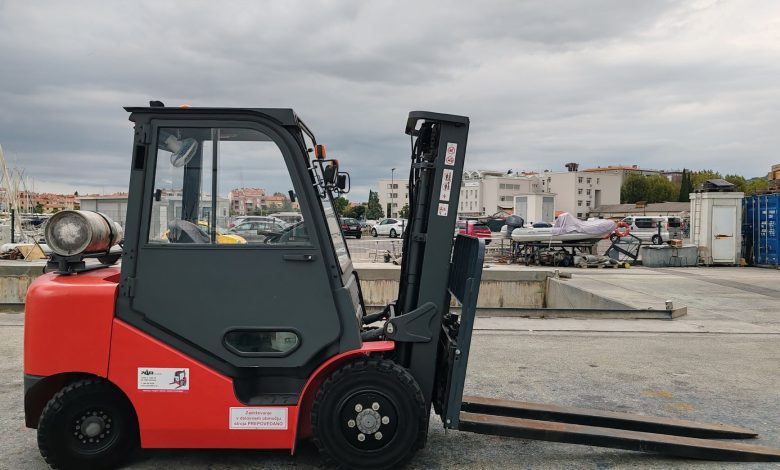 Red industrial forklift parked in a dockyard with urban background.