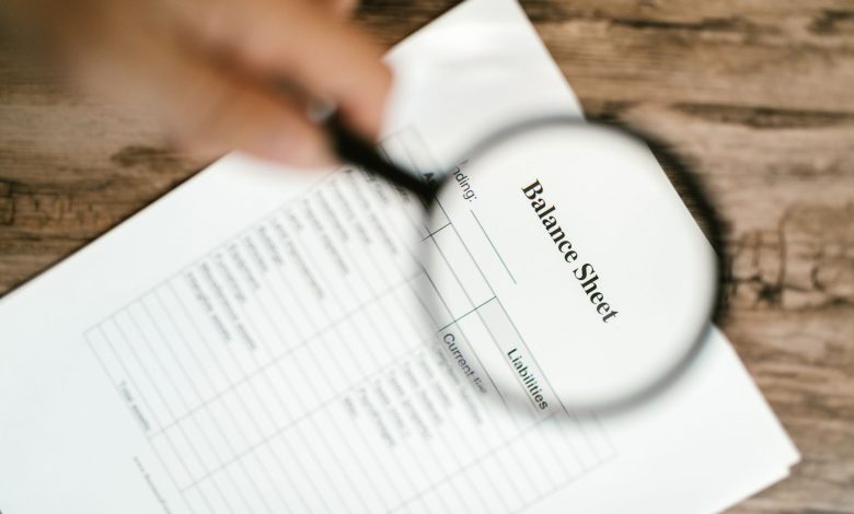 Close-up of a balance sheet under a magnifying glass on a wooden table.