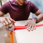 A man applying tape to a cardboard box for moving indoors.