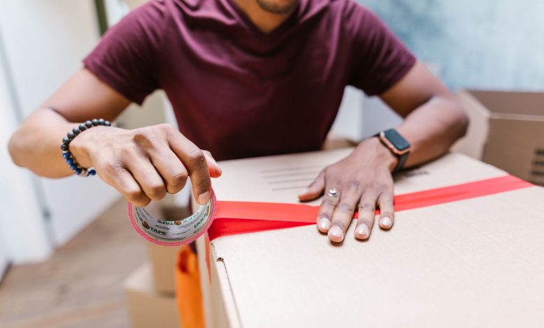 A man applying tape to a cardboard box for moving indoors.