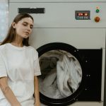 A woman in a laundry facility standing by a washing machine, contemplating the process.