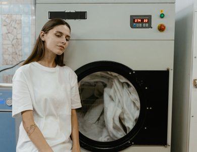 A woman in a laundry facility standing by a washing machine, contemplating the process.