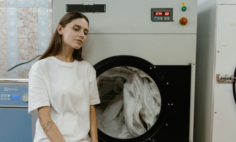 A woman in a laundry facility standing by a washing machine, contemplating the process.